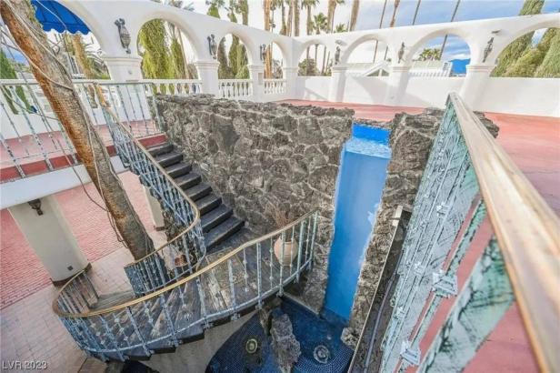 Blick auf eine Treppe mit Wasserfall in einem Gebäude mit weißer Fassade und Bögen.