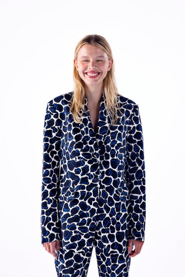 Eine lächelnde Frau trägt einen blau-weiß gemusterten Blazer und eine passende Hose.