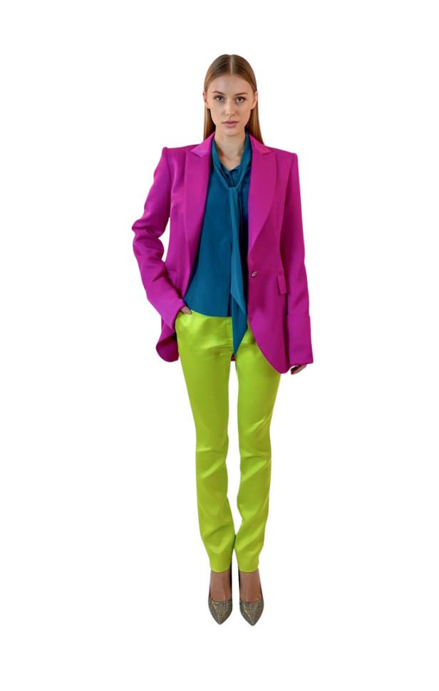 Eine Frau in einem pinkfarbenen Blazer und einer hellgrünen Hose posiert.