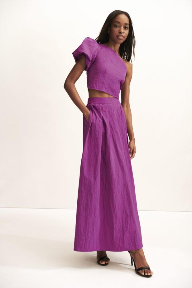 Eine Frau in einem violetten, einteiligen Kleid mit einem offenen Schulterdesign und einem langen Rock.