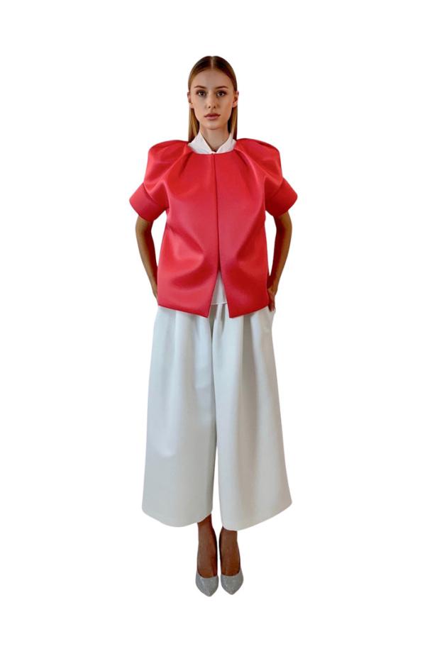 Eine Frau trägt eine rote Jacke mit Puffärmeln und eine weiße Culotte.