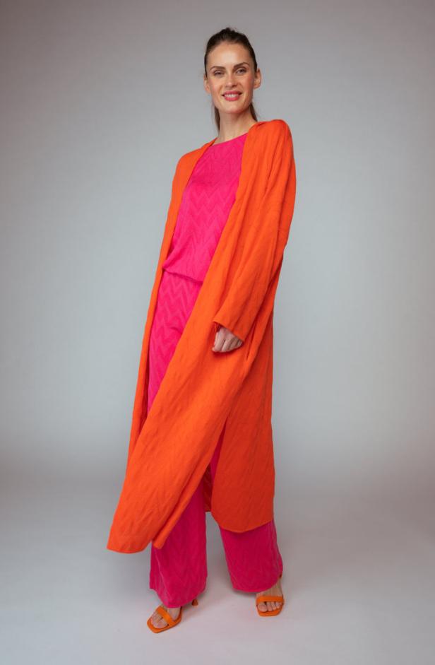 Eine Frau trägt ein pinkes Ensemble mit einem langen, orangefarbenen Cardigan.