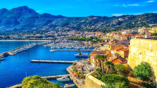 Blick auf Calvi, Korsika, mit dem Hafen voller Boote und den Bergen im Hintergrund.