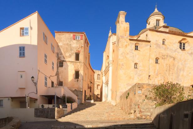 Eine Gasse mit Treppen führt zu einer Kirche in einer mediterranen Stadt.