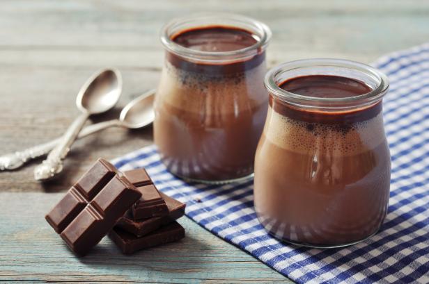 Zwei Gläser Schokoladenpudding stehen neben Schokoladenstücken auf einem Küchentuch.