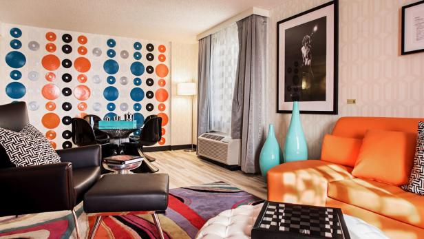 Ein Wohnzimmer mit einem orangefarbenen Sofa, einem Esstisch und einer Wand mit Schallplattenmuster.