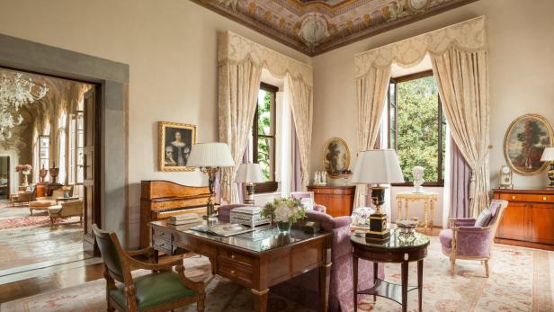 Ein elegantes Arbeitszimmer mit antiken Möbeln, Gemälden und einem Schreibtisch mit Glasplatte.