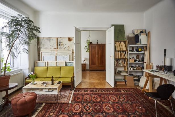 Ein Wohnzimmer mit einem gelben Sofa, einem roten Teppich und einem offenen Durchgang zu einem anderen Raum.