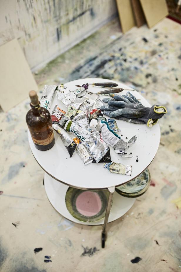 Ein Tisch mit Farbtuben, Pinseln, einer Flasche und Handschuhen in einem Atelier.
