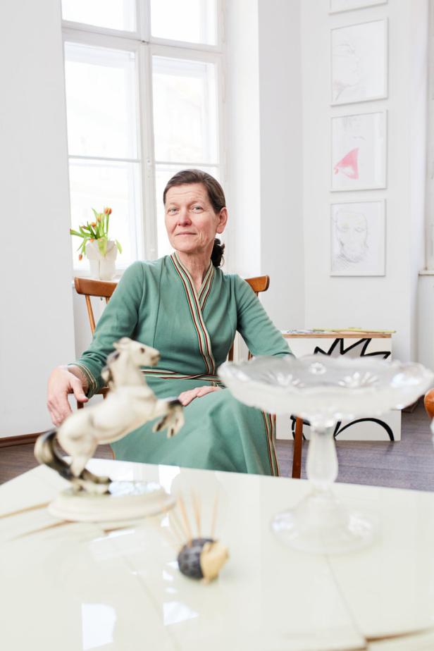 Eine Frau sitzt in einem grünen Kleid in einem hellen Raum mit Kunstwerken.