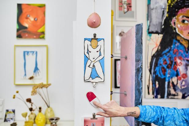 Eine Hand zeigt auf eine rote und weiße Kapsel, die an einer Wand mit Kunstwerken befestigt ist.