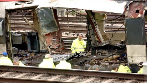 Ein Mann in gelber Jacke telefoniert vor einem zerstörten Zug.