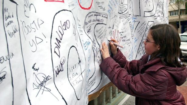 Ein Mädchen schreibt auf ein großes Plakat mit der Aufschrift „Basta Ya!“.