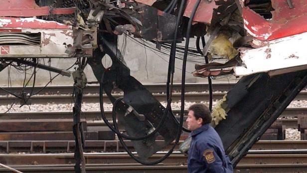 Ein Mann in Uniform steht vor den Trümmern eines Zuges auf einem Gleisbett.