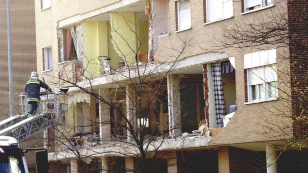 Ein Feuerwehrmann auf einer Drehleiter vor einem beschädigten Wohnhaus.