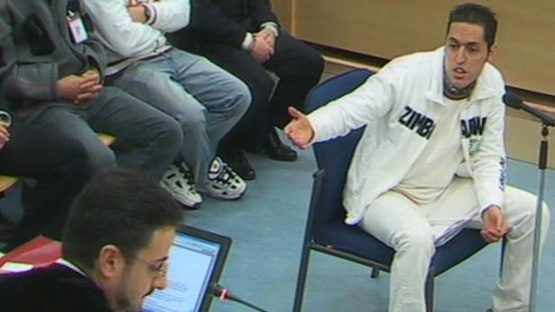 Ein Mann in weißer Kleidung gestikuliert während einer Gerichtsverhandlung.