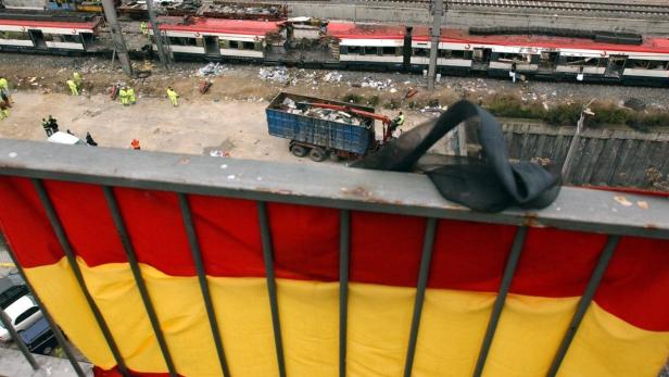 Blick von einem Balkon mit spanischer Flagge auf die Aufräumarbeiten nach einem Zugunglück.