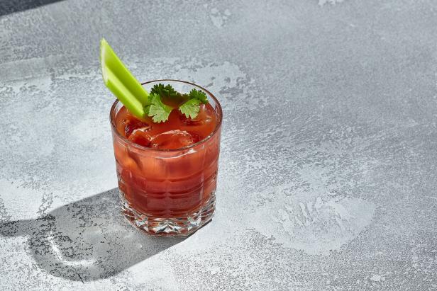 Ein Glas Bloody Mary mit Sellerie und Eiswürfeln auf einem grauen Tisch.