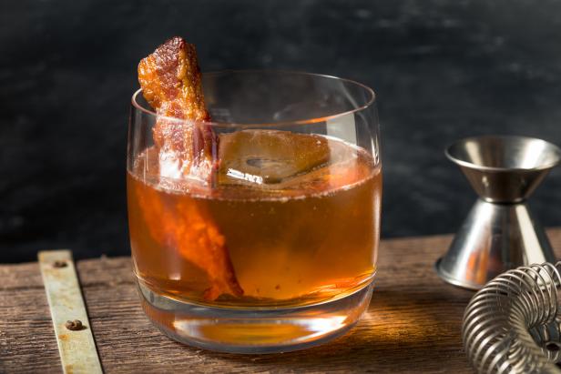 Ein Cocktail mit Eis und Speckgarnitur auf einem Holzbrett.