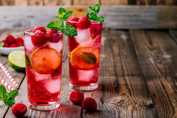 Zwei Gläser Himbeerlimonade mit Eis, Limette und Minze auf einem Holztisch.