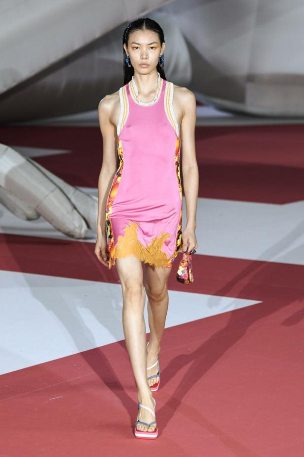 Eine Frau in einem pinkfarbenen Kleid mit floralen Details auf einem Laufsteg.