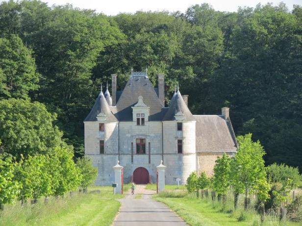 Ein kleines Schloss mit Türmchen und rotem Tor, umgeben von Bäumen.