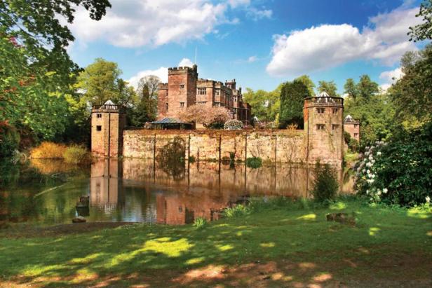 Ein von einem Wassergraben umgebenes Schloss aus rotem Backstein unter blauem Himmel.