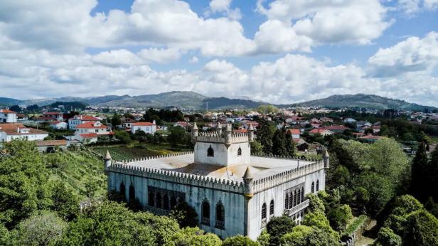 Ein Schloss mit Zinnen steht vor einer Stadtlandschaft mit Bergen im Hintergrund.