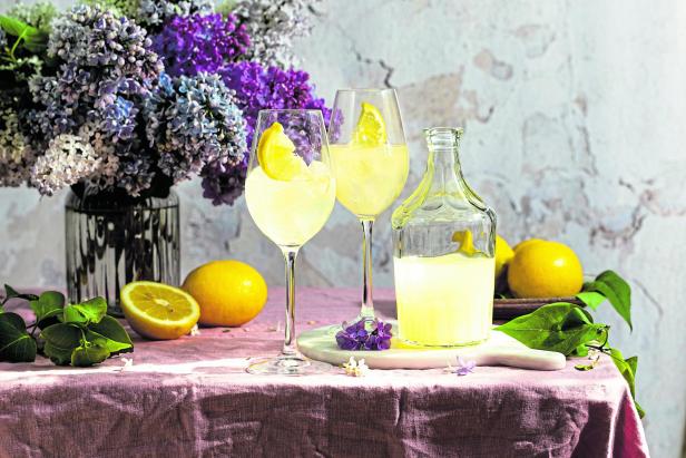 A bottle of Italian traditional liqueur limoncello with glasses, lemons and a vase with blooming lilac