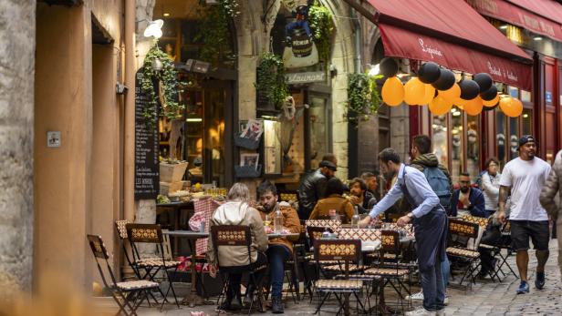 Ein belebtes Restaurant im Freien mit Gästen und einem Kellner in Lyon, Frankreich.