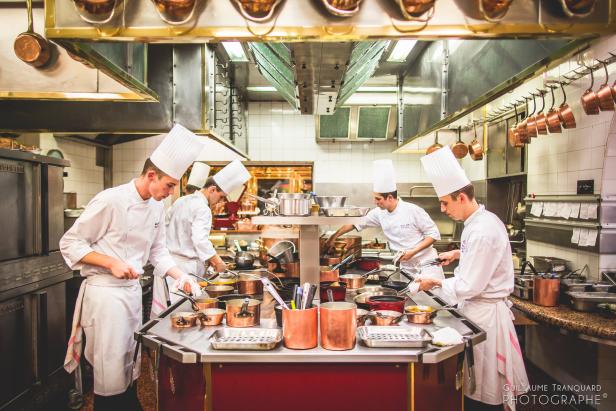Mehrere Köche bereiten Speisen in einer professionellen Restaurantküche zu.