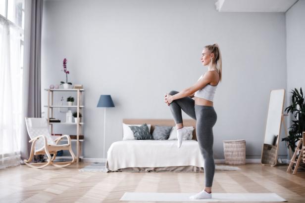 Eine Frau dehnt sich in einem hellen Raum auf einer Yogamatte.