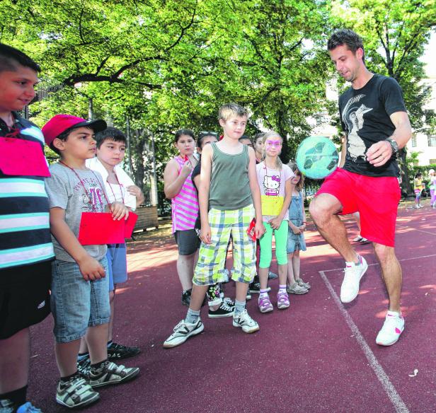 Ein Mann jongliert einen Ball vor einer Gruppe von Kindern im Freien.