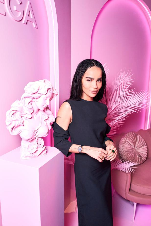 Zoë Kravitz posiert vor einem rosa Hintergrund mit einer Büste und einem Sessel.