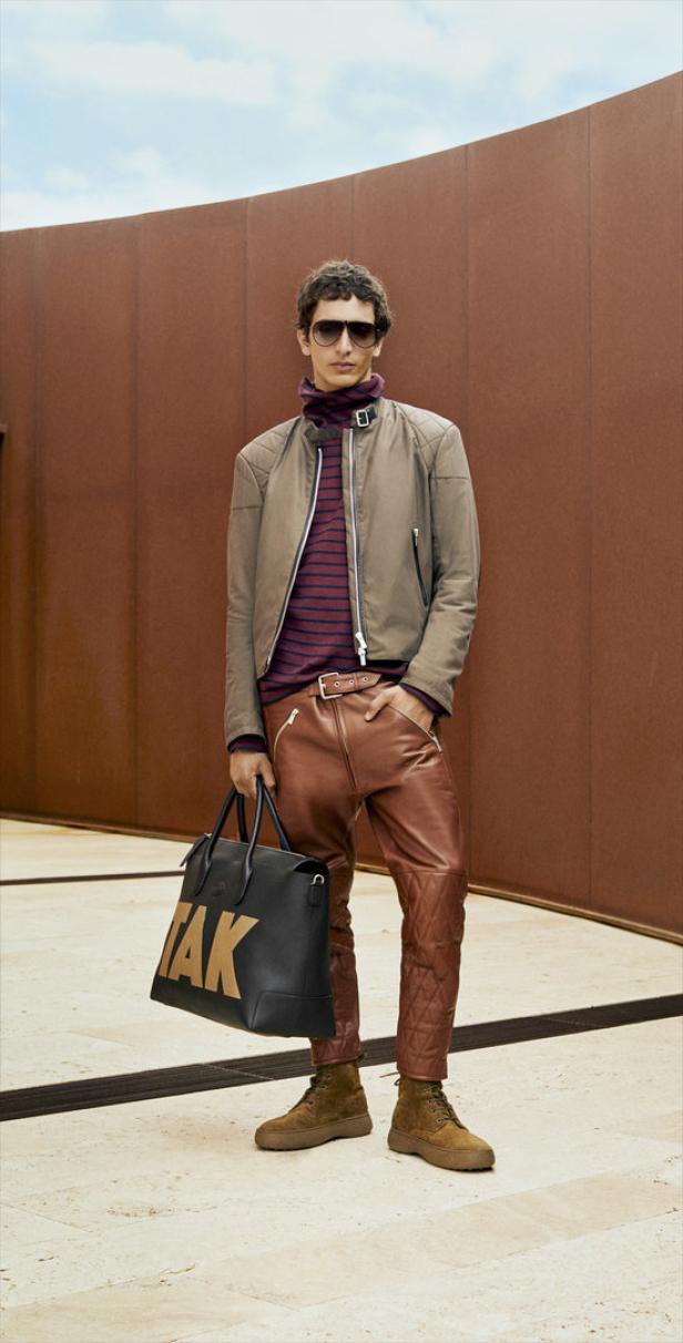 Ein Mann mit Sonnenbrille, Lederhose und Jacke hält eine schwarze Tasche.