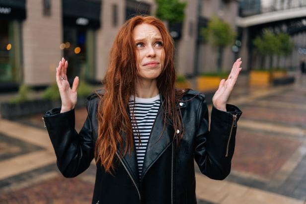 Eine Frau mit roten Haaren steht im Regen und wirkt ratlos.