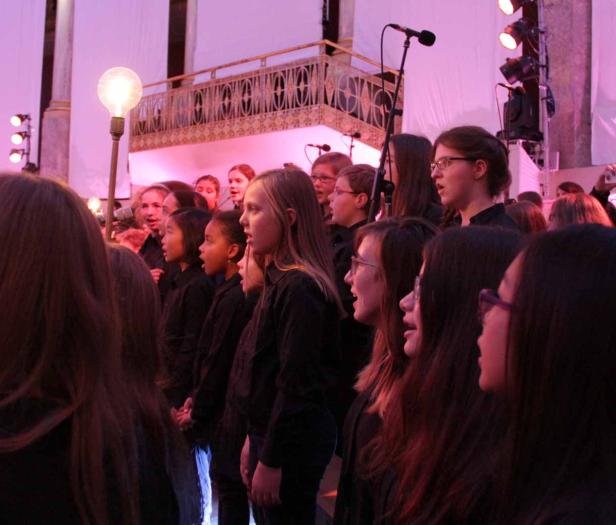 Ein Kinderchor singt auf einer Bühne mit rosa Beleuchtung.