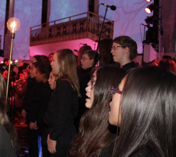 Ein Jugendchor singt auf einer Bühne mit roter Beleuchtung.