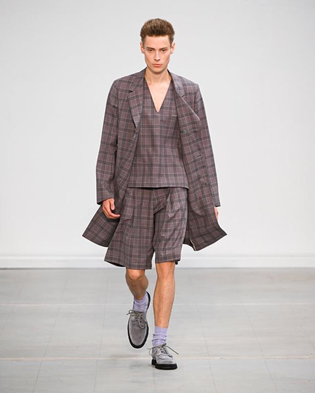 Ein Mann präsentiert ein kariertes Ensemble aus Blazer, Top und Shorts auf einem Laufsteg.