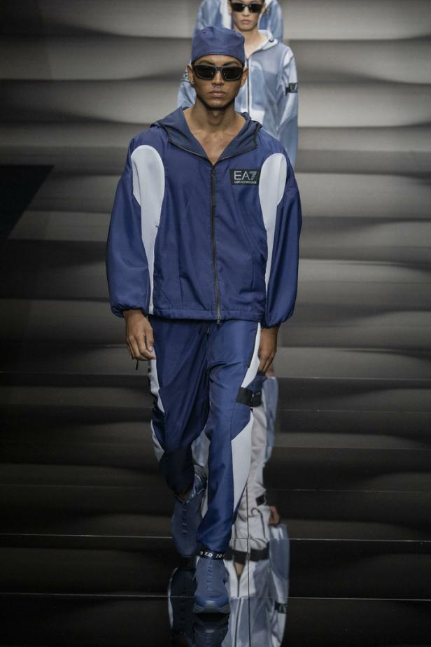 Ein Model auf dem Laufsteg, gekleidet in einem marineblauen Trainingsanzug von EA7 mit weißen Akzenten.