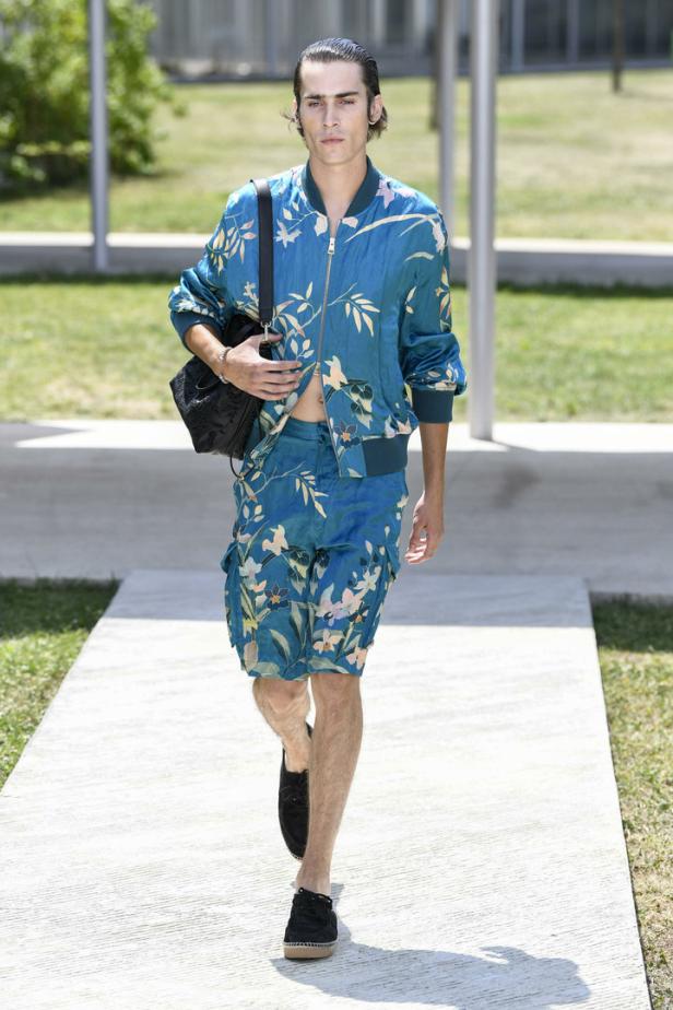 Ein Mann in einem blaugrünen, floral gemusterten Outfit läuft auf einem Gehweg.