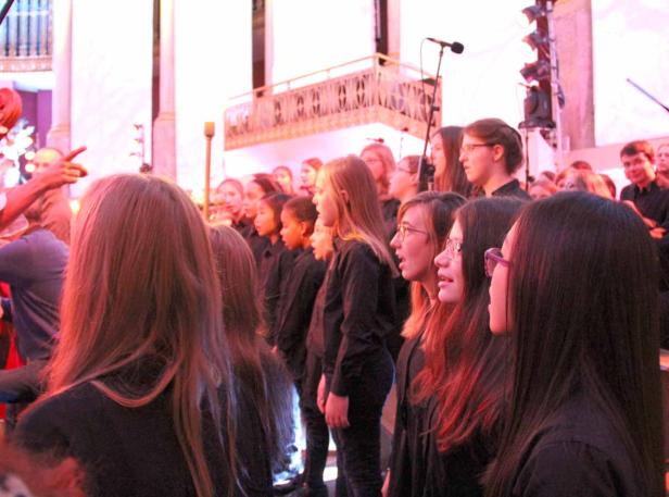 Ein Chor singt in einem großen Saal mit einem Dirigenten.