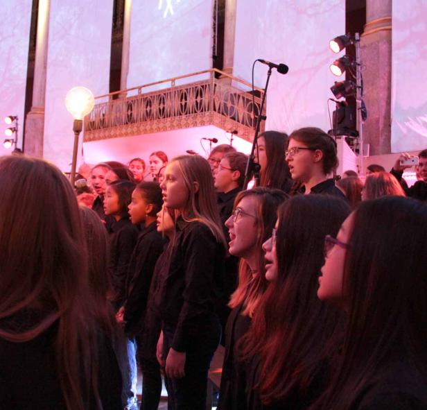 Ein Jugendchor singt auf einer Bühne mit roter Beleuchtung.
