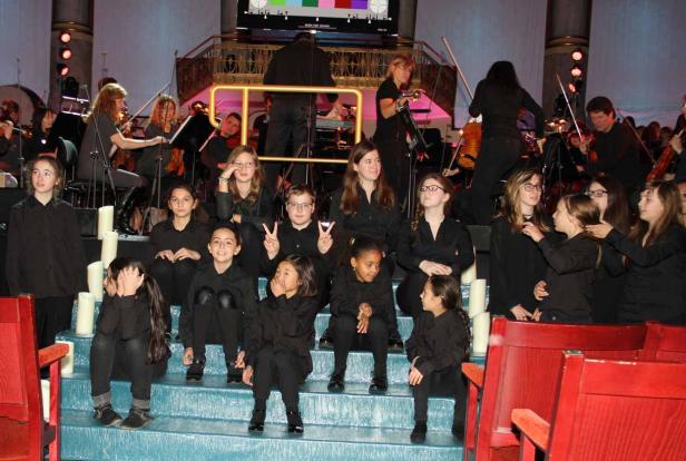 Eine Gruppe von Kindern sitzt vor einem Orchester auf einer Treppe.