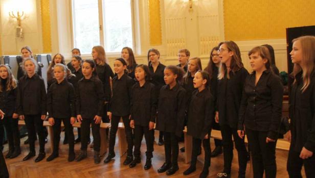 Ein Mädchenchor singt in einem Raum mit gelben Wänden.