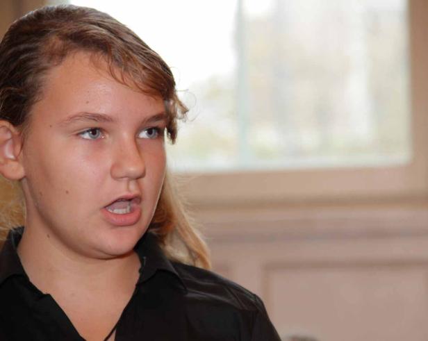 Eine junge Frau mit hellblauen Augen und dunklem Hemd spricht.