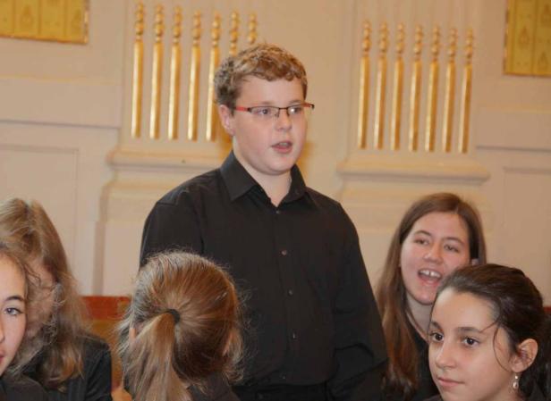 Ein junger Mann mit Brille singt vor einer Gruppe von Zuhörern.