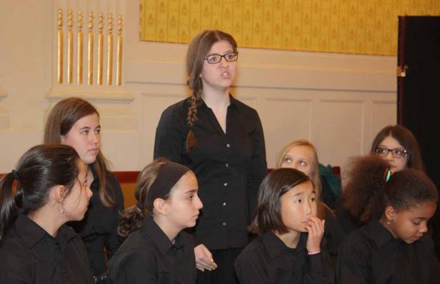 Eine junge Frau spricht vor einer Gruppe von Mädchen, die schwarze Hemden tragen.