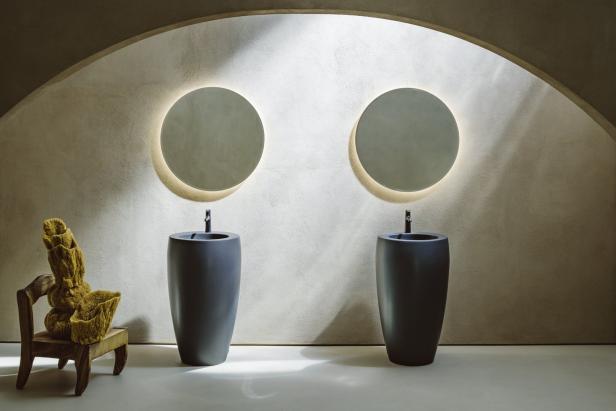 Ein Badezimmer mit zwei runden Spiegeln über freistehenden Waschbecken und einem Schwamm auf einem Stuhl.