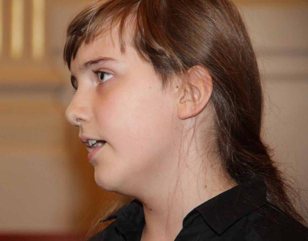 Ein junges Mädchen mit braunen Haaren und einem schwarzen Hemd im Profil.